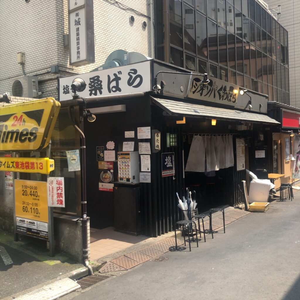 池袋にある塩そば専門店 桑ばらの店舗外観。白い看板と黒い外壁、券売機と暖簾が特徴的な路面店。