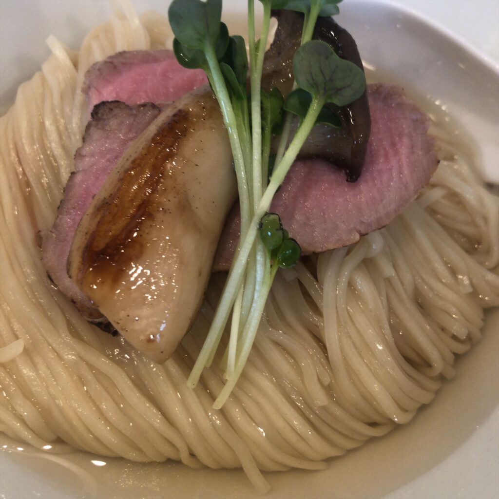 ぬまちゃんラーメンの「つけめん澄み」。昆布水に浸った中細麺の上に、ソテーされたエリンギと低温調理チャーシュー、いわれ大根が美しく盛り付けられている。