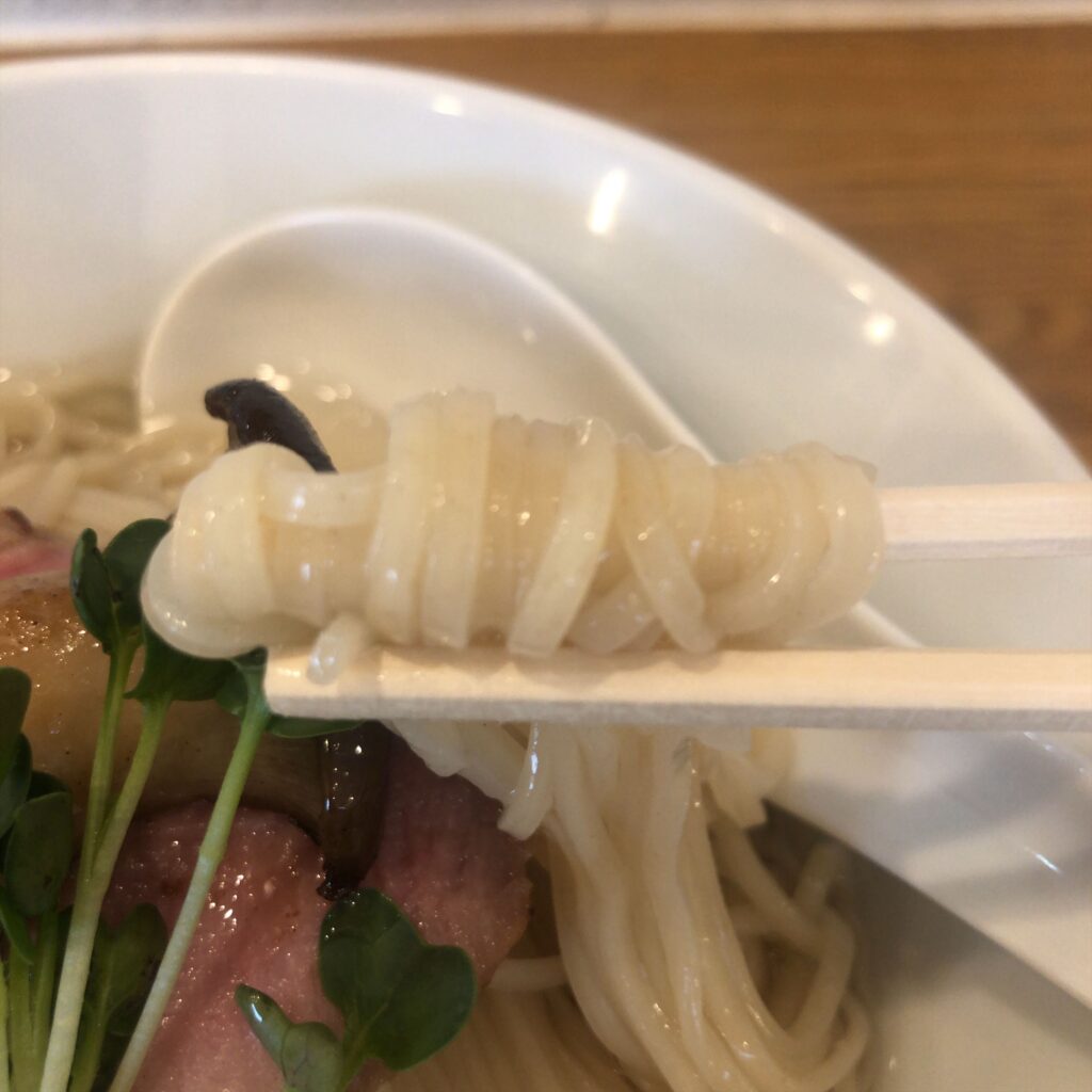 ぬまちゃんラーメンの「つけめん澄み」。昆布水に浸かった中細麺を箸で持ち上げた様子。透明感のあるとろみが絡み、滑らかな質感が際立つ。