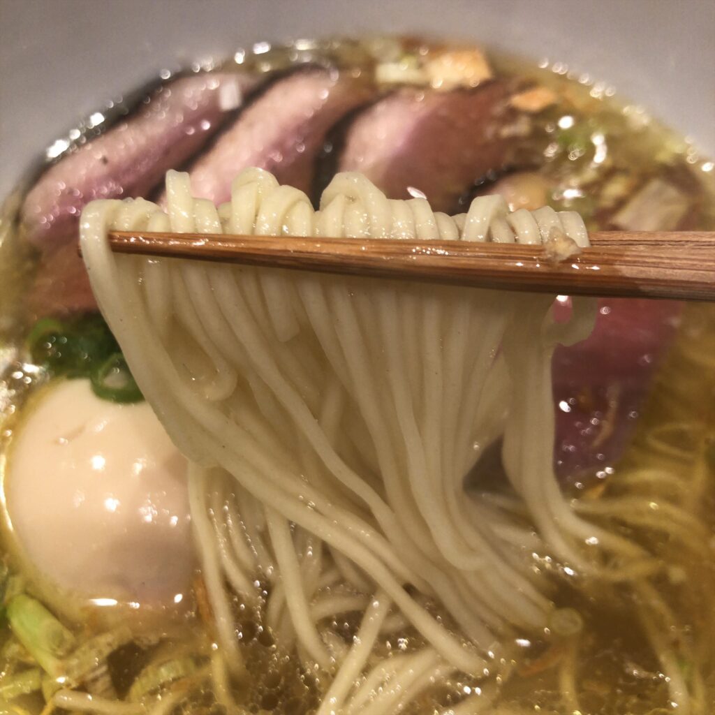 Ramen翡翠の鴨山椒塩ラーメンを箸で持ち上げた細麺のアップ。透き通るスープとしなやかなストレート麺。