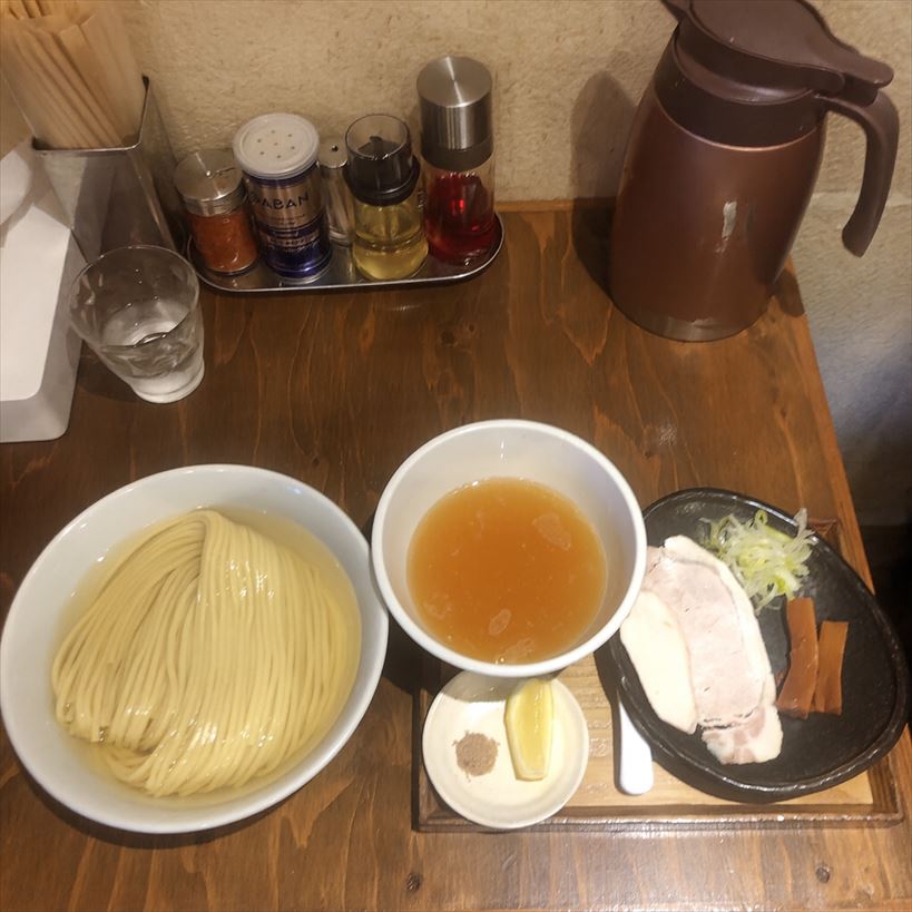 麺屋鈴春の昆布水つけ麺セット。昆布水に浸かった麺、澄んだ醤油つけ汁、レアチャーシューやメンマ、ネギ、レモンと藻塩の味変が木製トレイに並ぶ。