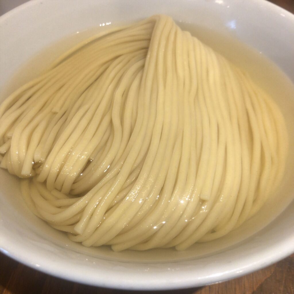 麺屋鈴春の昆布水つけ麺。透明感のある昆布水に艶やかな中太麺が丁寧に折りたたまれて盛り付けられている。