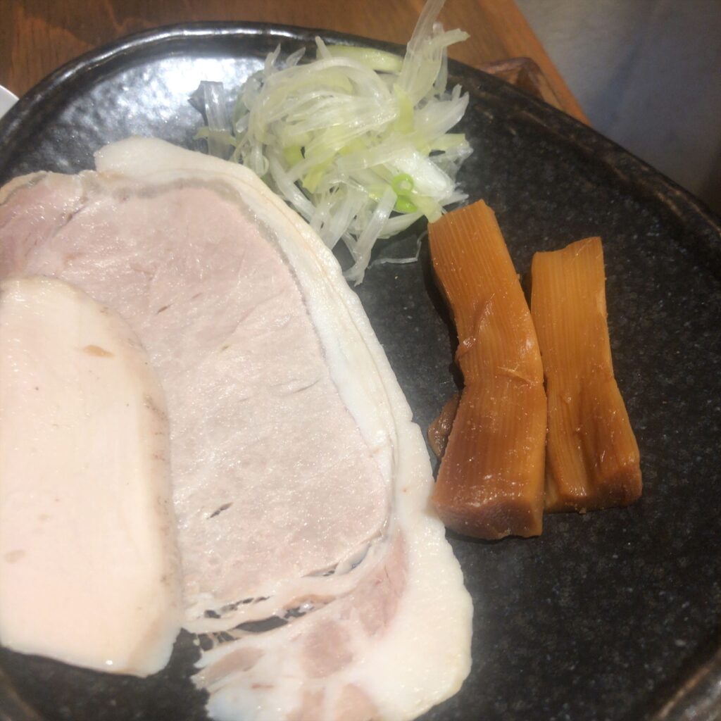 麺屋鈴春のトッピング盛り。豚と鶏のレアチャーシュー、穂先メンマ、刻みネギが黒い皿に美しく並べられている。