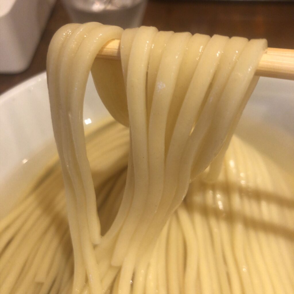 昆布水に浸かった麺を箸で持ち上げた様子。艶やかで弾力のある麺が光って見える。