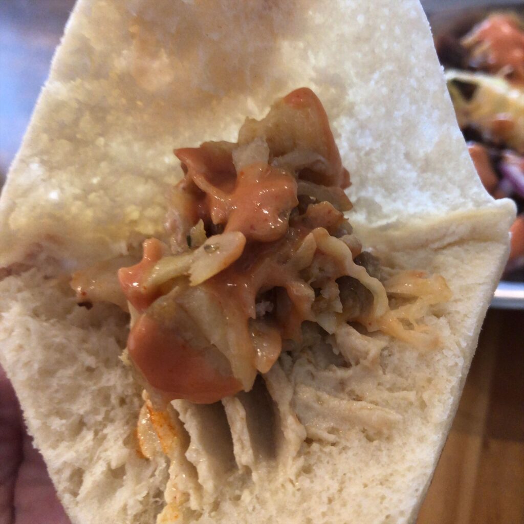 HISAR（ヒサル）飯田橋店で、ピタパンにビーフとチキンのケバブを包み、フムスを添えた一口。